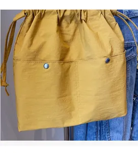 Detail of ginger yellow nylon bucket bag showing drawstring closure and front pockets