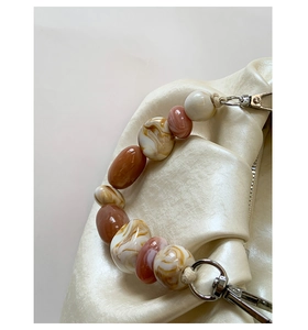 Detail of creamy white ruched handbag featuring a marbled acrylic bead handle and silver metal clasp