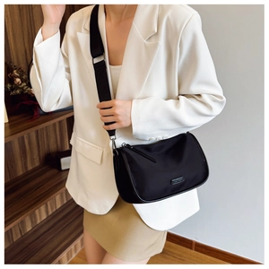 Gros plan d'un sac bandoulière en toile noire avec large bandoulière porté par un mannequin