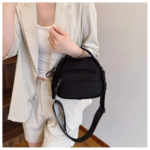 Close-up of black nylon shoulder bag with zipper pocket, styled with a beige suit
