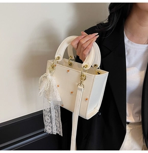 Detail of white textured mini tote with daisy embroidery and pearl lace bow strap