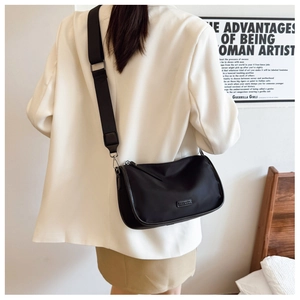 Vue détaillée du sac bandoulière en nylon noir avec sangle large sur blazer blanc