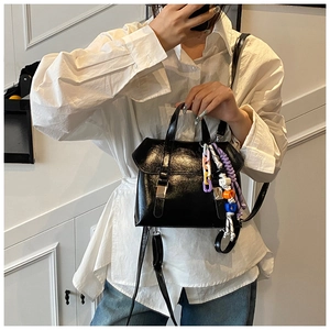 Detail of glossy black faux leather mini backpack with colorful woven charm accessory
