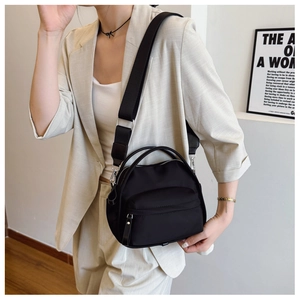 Close-up of a black minimalist crossbody bag with an adjustable wide strap and top handle