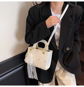 Detailed view of white mini handbag featuring daisy embroidery and pearl lace pendant charm