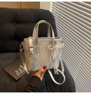 Details der silbernen Eimer-Tasche mit Schlangenprägung, Schleife und Perlenanhänger