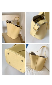 Detail view of pale yellow bucket bag showing leather texture, strap buckle and base rivets