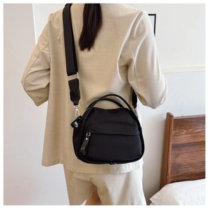 Detail of black crossbody bag with wide strap worn over a white blazer for modern style