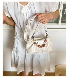 Detail view of a cream pleated bucket bag with decorative marble beads and strap
