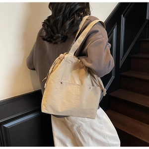 Detailed side view of a beige nylon bucket bag with drawstring and silver rivet pockets