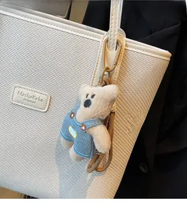 Detail eines Plüschbären-Anhängers mit blauer Latzhose an einer weißen Stepptasche