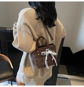 Detailstruktur der braunen Trapez-Handtasche mit weißem Spitzenbogen-Anhänger am Model