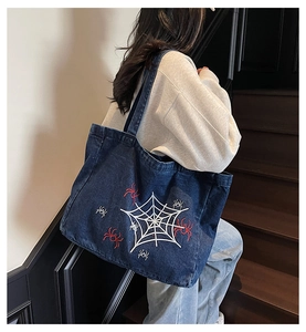 Detail of dark blue denim tote bag featuring white spider web and red spider embroidery