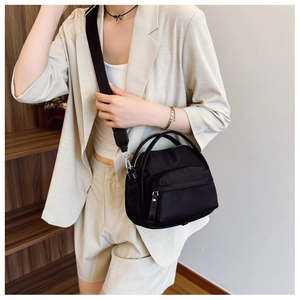 Close-up of black nylon crossbody bag with wide shoulder strap and silver metal zippers