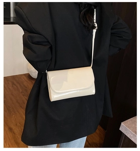 Detail van de crème glanzende leren crossbodytas gestyled met een zwarte blazer