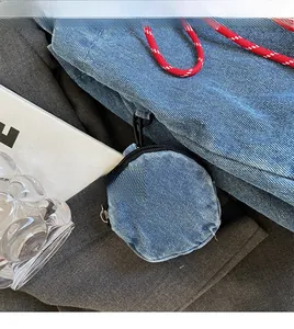 Close-up of a small round denim coin purse with a black zipper and metal snap hook