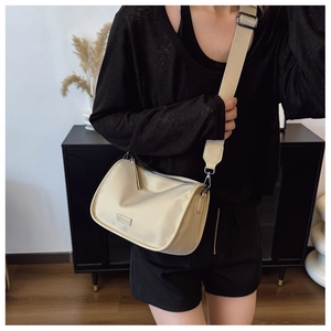 Détail du sac bandoulière beige avec large sangle et plaque métallique de logo