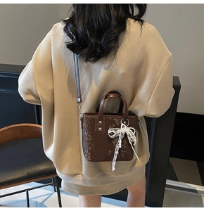 Braune strukturierte Beuteltasche mit Spitzenperlenbogen-Anhänger am Modell getragen