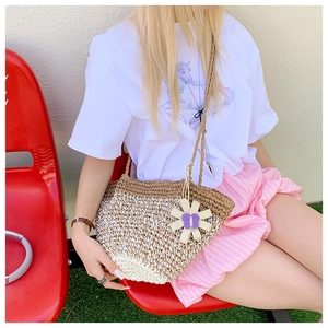 Detail of handmade straw shoulder bag with floral charm and woven strap on a model