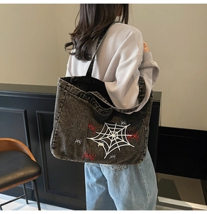 Detail view of large grey denim tote bag with spider embroidery worn by a model