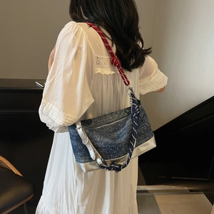 Detail of blue denim tote bag with red and blue woven rope shoulder strap and silver trim