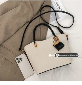 Close-up of beige woven tote bag with black handles and an iPhone 12 for size reference