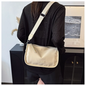 Détail d'un sac bandoulière en toile crème avec large sangle porté par un mannequin