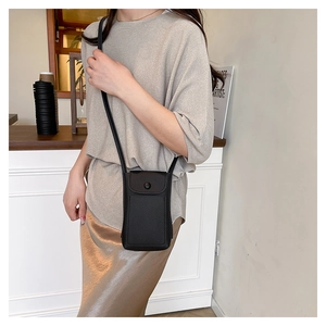 Model wearing a minimalist black litchi leather mini crossbody bag with a slim strap