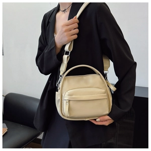 Detail of beige crossbody bag with wide strap on model in black suit for casual style