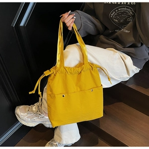 Detail of bright yellow nylon drawstring tote bag featuring silver decorative snap buttons