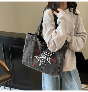 Detail of a large denim tote bag featuring white spider web embroidery and washed black finish