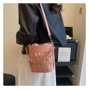 Detail of pink hollow-out bucket bag featuring silver rivets and a canvas drawstring pouch