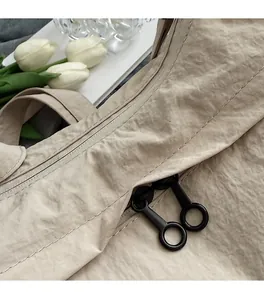 Detail of fine white stitching on a beige nylon shoulder bag with dual black zippers