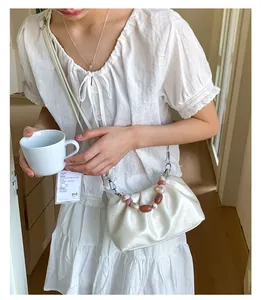 Detail of white pleated cloud bag featuring marble beads on handle and shoulder strap