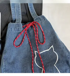 Detail of blue denim tote bag featuring white cat embroidery and red-white drawstring