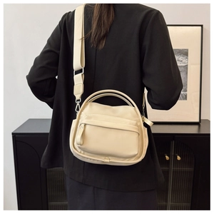 Rear view of minimalist off-white crossbody bag with multiple zippers and wide strap