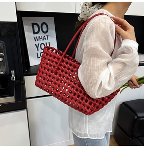 Detail of red woven hollow-out tote bag showing glossy texture and shoulder strap on model