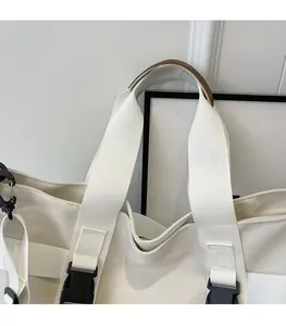 Detail view of large white canvas tote bag with brown leather handles and sturdy buckles