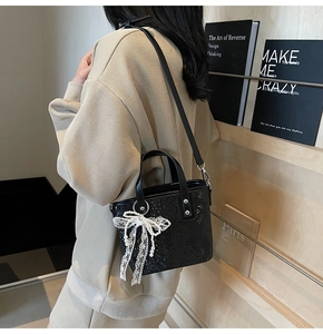 Detail der schwarzen Handtasche mit Schlangenprägung und dekorativer Spitzen-Perlen-Schleife