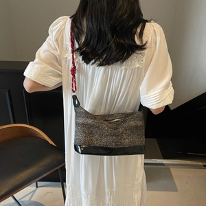 Detail of gray canvas crossbody bag with black patent leather bottom and red rope strap