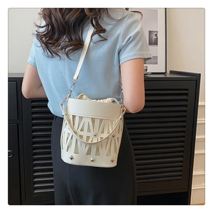 Detail of white hollowed-out bucket bag with metallic rivets and drawstring inner pouch