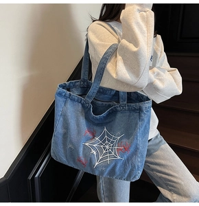 Detail of blue denim tote bag featuring intricate white spider web and red spider embroidery