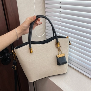 Detail of beige woven tote bag with black leather trim, gold hardware, and mini charm