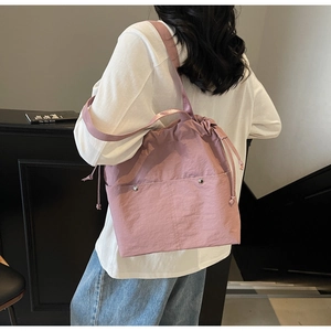 Model wearing a dusty pink nylon drawstring bucket bag with a wide shoulder strap