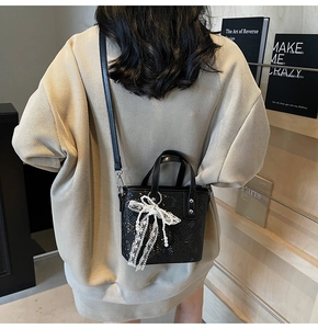 Detailansicht einer schwarzen Eimer-Tasche mit Schlangenhautmuster und Spitzen-Schleife