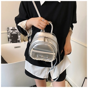 Detail eines silbernen Metallic-Minirucksacks mit weißem Spitzenbesatz und Schleifenakzent
