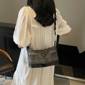 Detail of glitter fabric and black leather crossbody bag on a model wearing a white dress