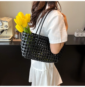 Close-up of black hollow woven beach bag with twin handles held by a model in white