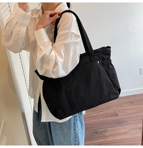 Modèle portant un grand sac cabas en toile noire avec cordons et détails de rivets