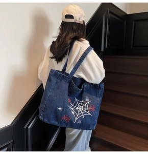Detail of navy denim tote bag with spider web embroidery worn on shoulder in street style